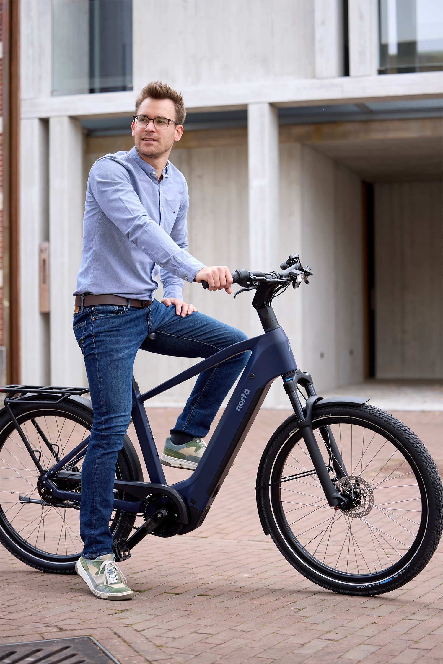 Een man staat klaar om te vertrekken naar zijn werk met zijn elektrische fiets met hoge instap. De kleur van de fiets is Steel Blue. 