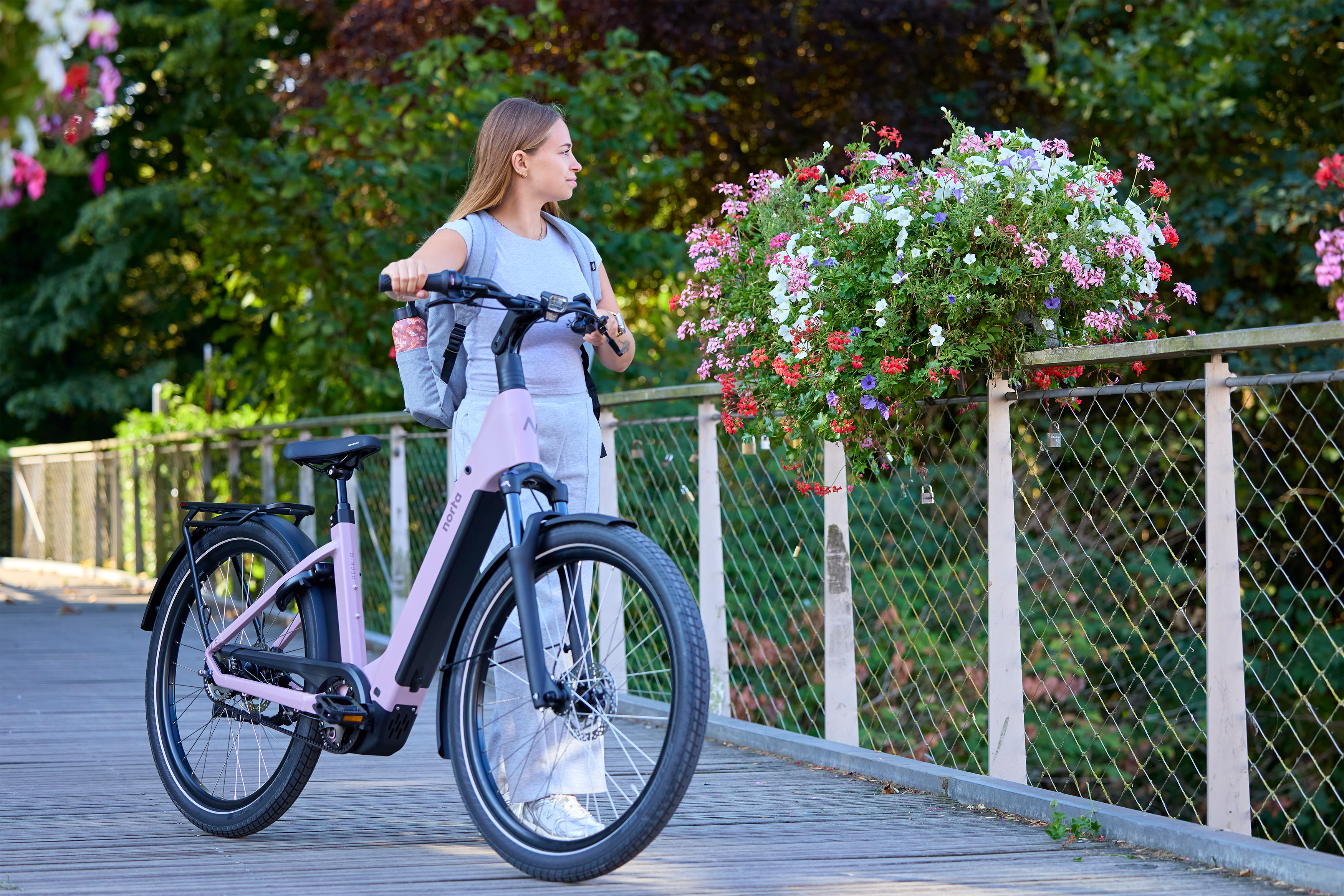 Vrouw staat op een brug naast haar pastel violet elektrische fiets met het logo van Norta.
