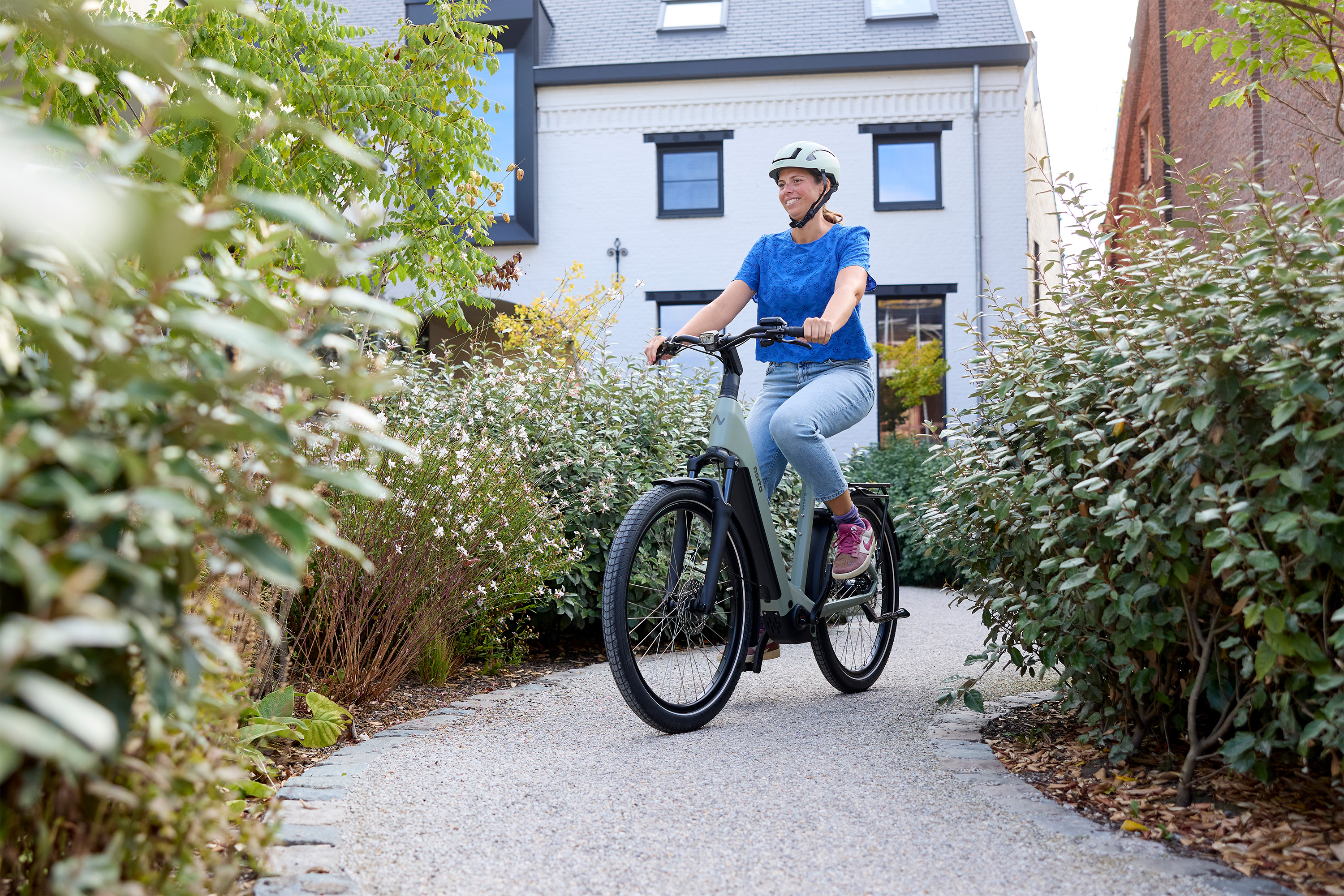 Vrouw met fietshelm rijdt op een elektrische fiets door een groene, rustige woonomgeving.