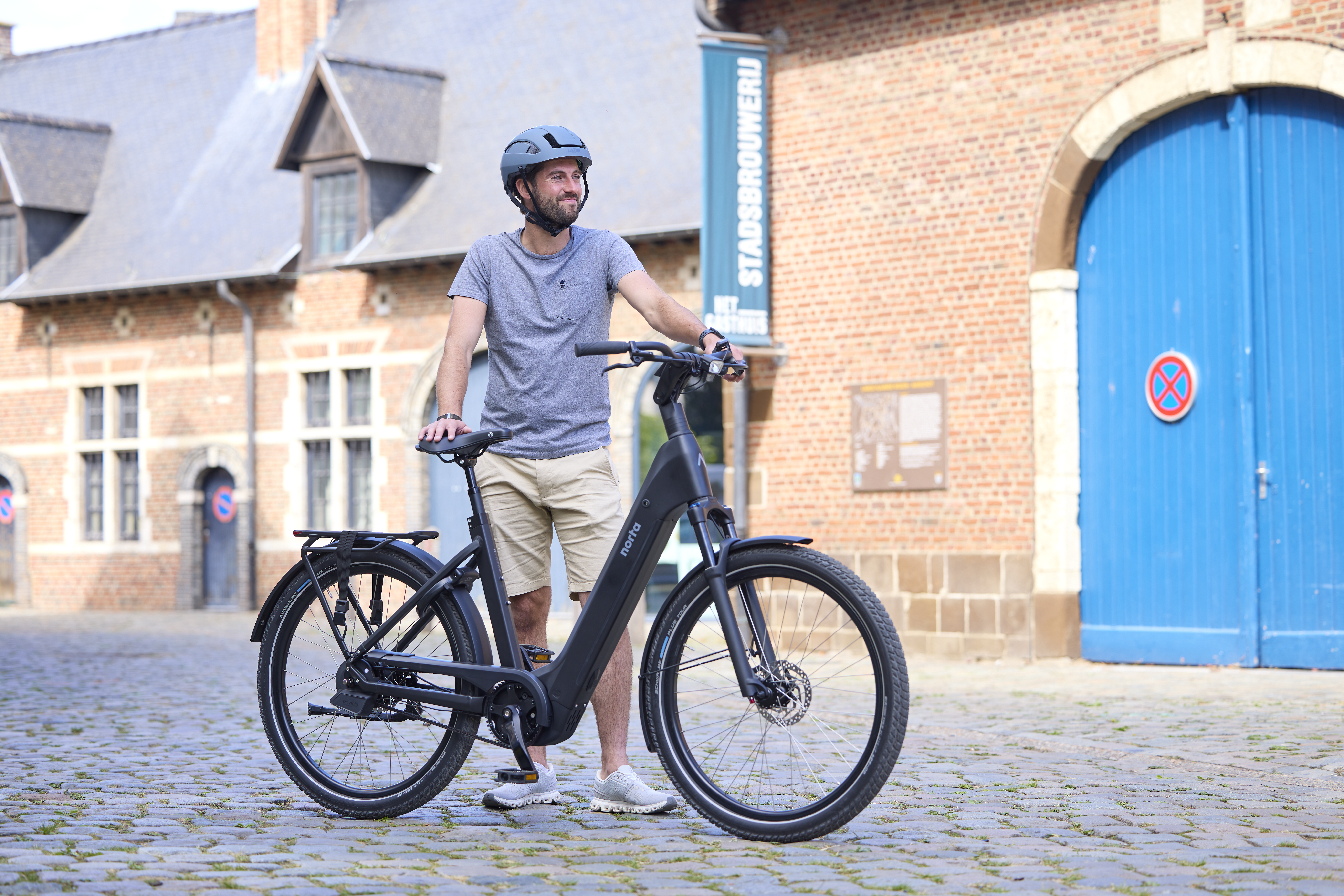 Man staat naast zijn zwarte fiets van Norta in een historische omgeving.